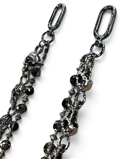 A close-up of a gothic-style metal chain accessory featuring skull charms, faceted black beads, and ornate links, shown against a plain white background.