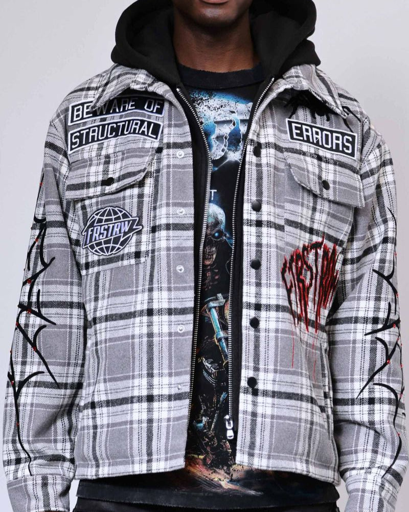 Person wearing a plaid jacket with patches and a graphic t-shirt on a gray background