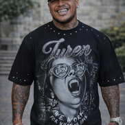 Person wearing a black graphic t-shirt with a stylized face design and text, standing outdoors.