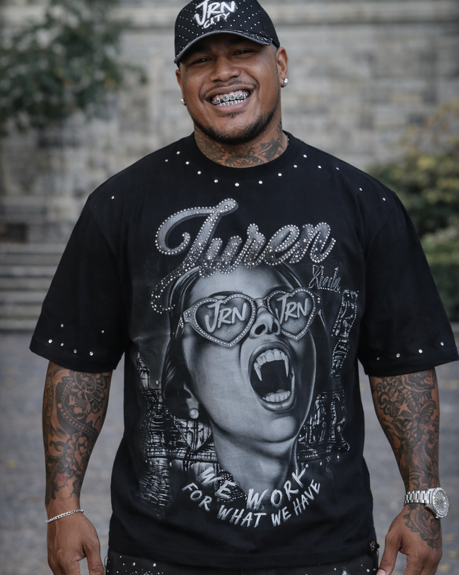 Person wearing a black graphic t-shirt with a stylized face design and text, standing outdoors.