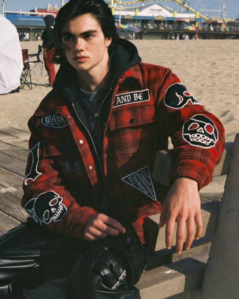 Person wearing a red plaid jacket with patches on a beach