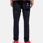 Person wearing black pants with a brand logo, brown shirt, and red shoes on a white background