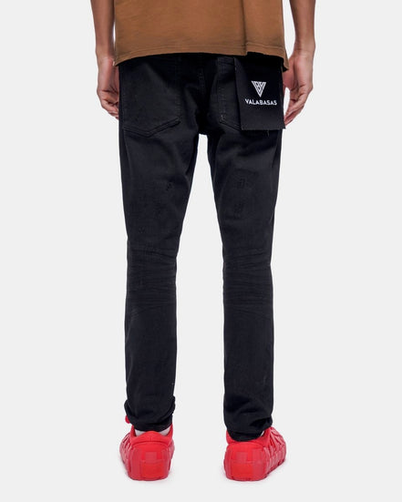 Person wearing black pants with a brand logo, brown shirt, and red shoes on a white background