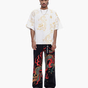Person wearing a white shirt with dragon design and black pants with red dragon design on a white background