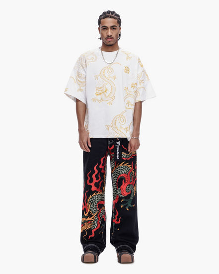 Person wearing a white shirt with dragon design and black pants with red dragon design on a white background