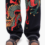 Black pants with red and green dragon design worn by a person on a white background