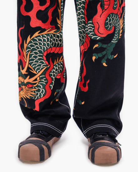 Black pants with red and green dragon design worn by a person on a white background