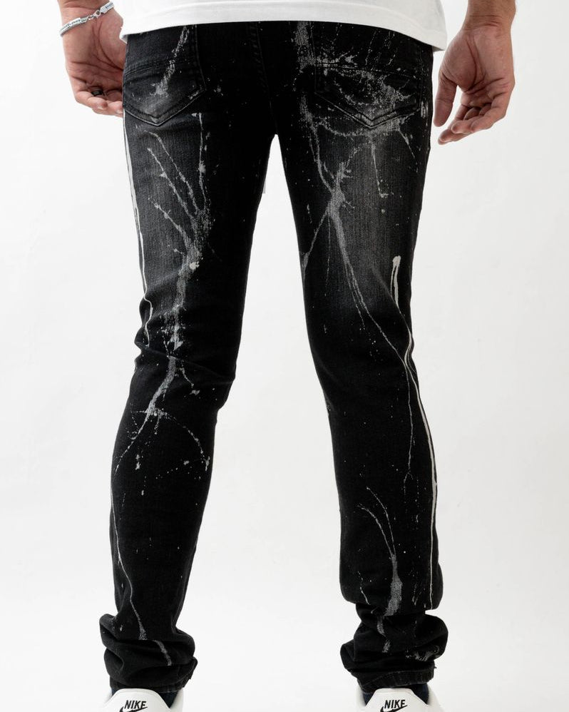 Person wearing black distressed jeans with white splatter design on a white background