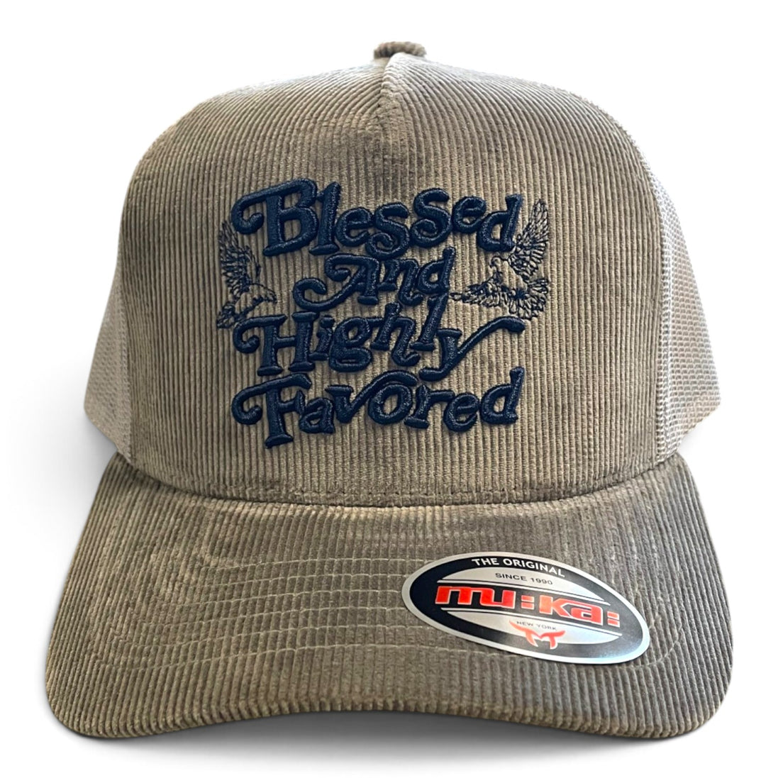 A beige corduroy trucker hat with navy blue embroidered text reading 'Blessed And Highly Favored' on the front, featuring a visible Muski brand sticker on the brim.