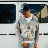 person wearing an all grey hoodie with religious imagery and rhinestone details. 