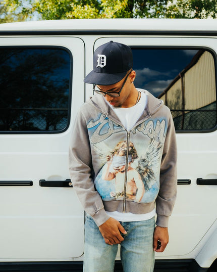 person wearing an all grey hoodie with religious imagery and rhinestone details. 
