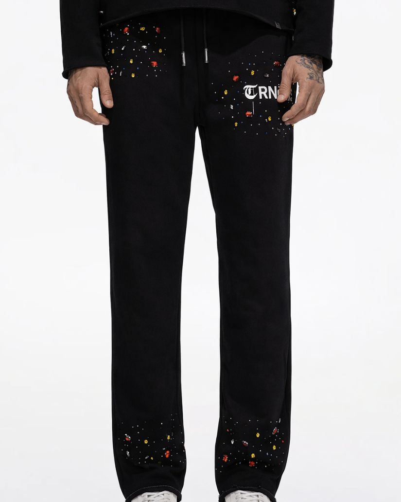 Person wearing black pants with colorful embellishments and a visible brand logo on a white background