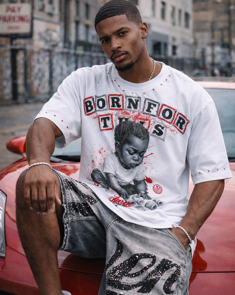 Man wearing a graphic t-shirt and shorts, sitting on a red car in an urban setting.