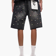 Person wearing black denim shorts with colorful studs on a white background