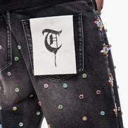 Black jeans with colorful embellishments and a white patch with a black symbol on the back pocket.