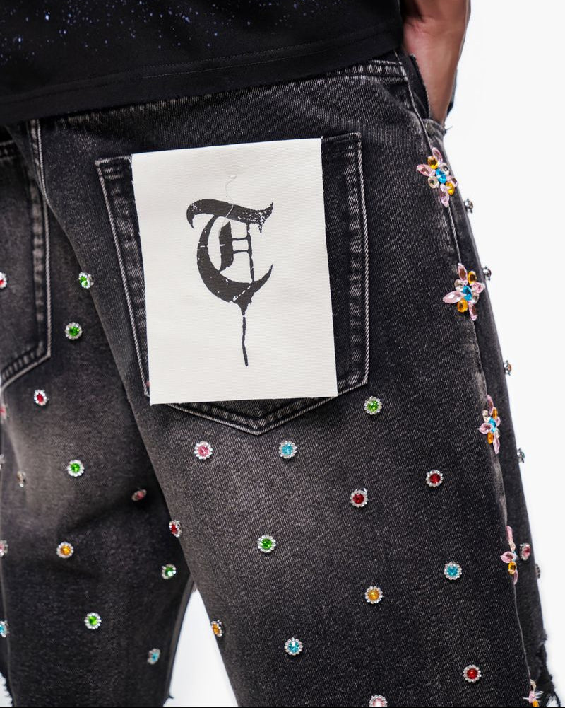 Black jeans with colorful embellishments and a white patch with a black symbol on the back pocket.