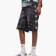 Person wearing black shorts with colorful patterns, a black t-shirt, white socks, and white sneakers on a white background.