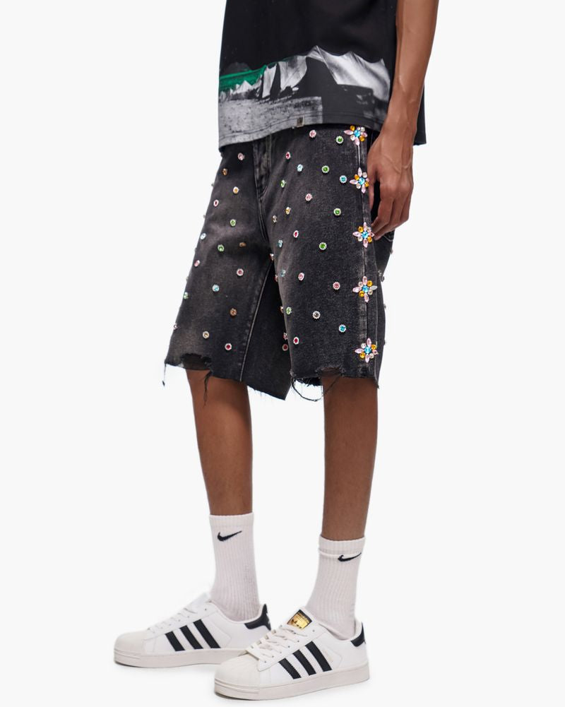 Person wearing black shorts with colorful patterns, a black t-shirt, white socks, and white sneakers on a white background.