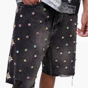 Black denim shorts with colorful embellishments worn by a person on a white background