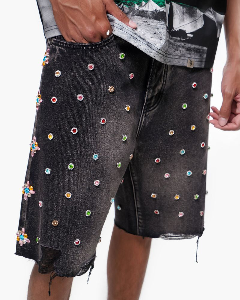 Black denim shorts with colorful embellishments worn by a person on a white background
