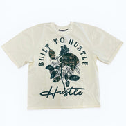 Beige t-shirt with floral design and 'Built to Hustle' text on a white background