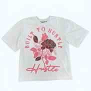 White t-shirt with pink floral design and 'Built to Hustle' text on a white background