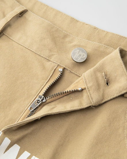 Close-up of a beige jacket with a zipper and button, featuring a coin and brand logo.