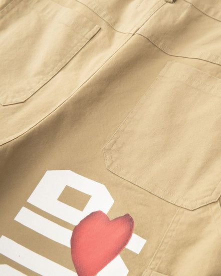 Close-up of beige pants with a brand logo and a red heart shape.