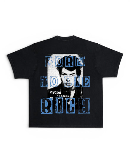 A black short-sleeve t-shirt with a graphic print on the back featuring a black-and-white portrait of One Direction's Nick Carter and the text 'BORN TO BE RICH' in distressed blue letters, with 'nycpd' printed below.