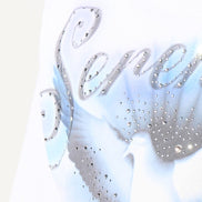 Close-up of a white garment with decorative text and embellishments on a light background