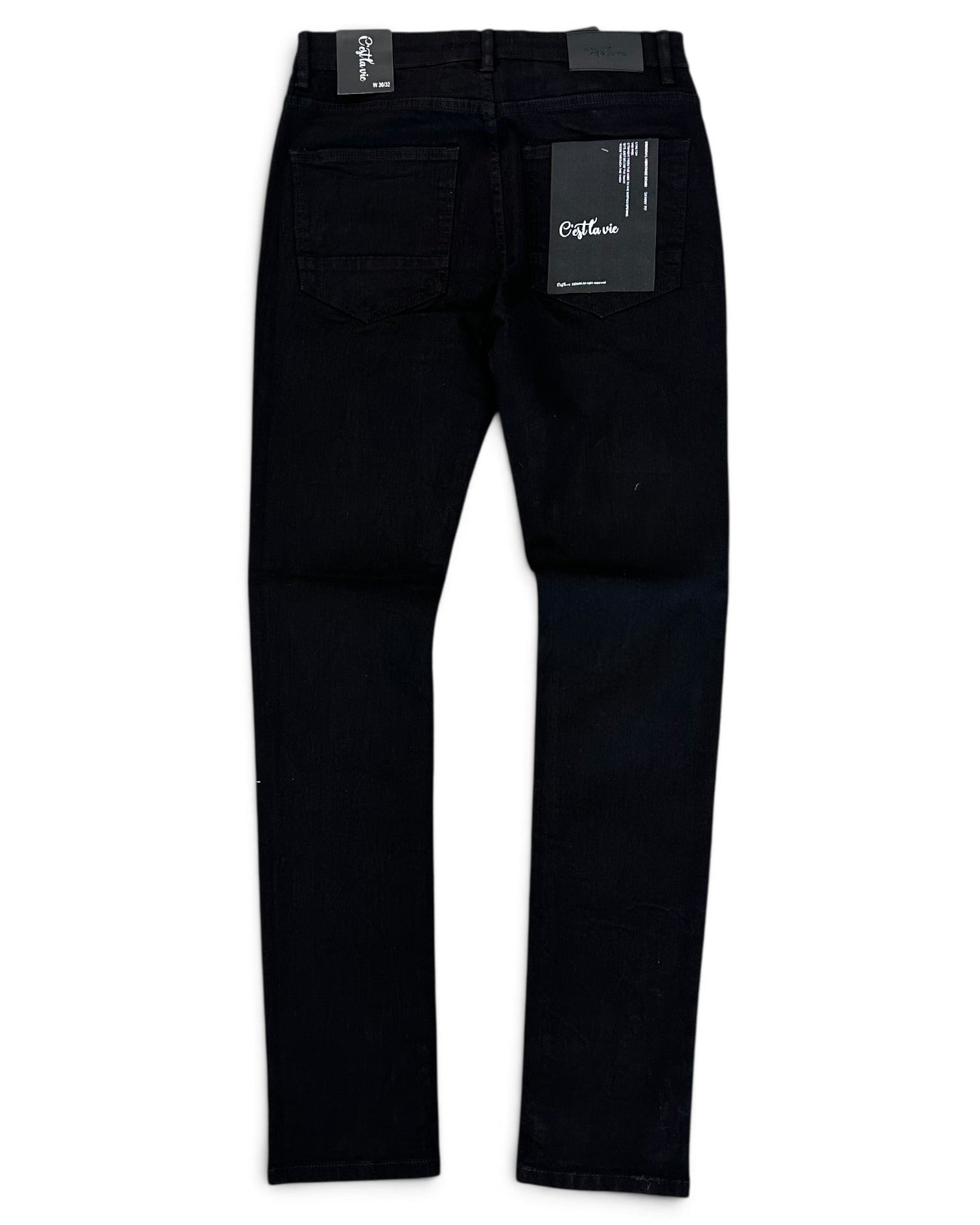 Black denim jeans shown from the back, featuring a black paper brand tag on the right side of the waistband and a black leather patch on the back waist, photographed against a plain white background.