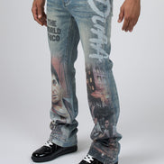 A person wearing blue denim jeans with large graphic prints and text, paired with black lace-up shoes, photographed against a light gray studio background.