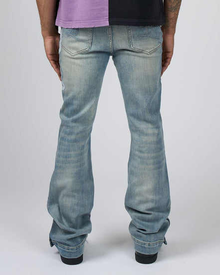 Rear view of a person wearing light-wash blue jeans with a split purple and black shirt, standing against a light gray studio background.