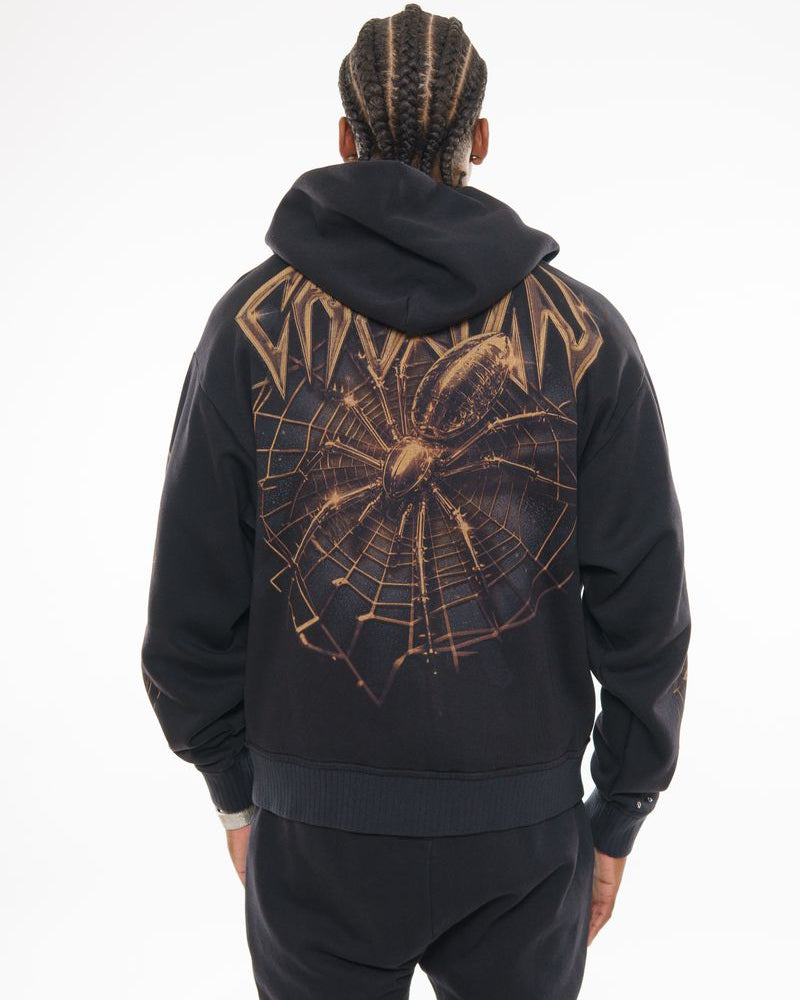 Person wearing a black hoodie with a spider web design on the back against a white background
