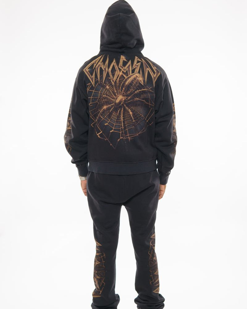 Person wearing a black hoodie and pants with spider web design on a white background