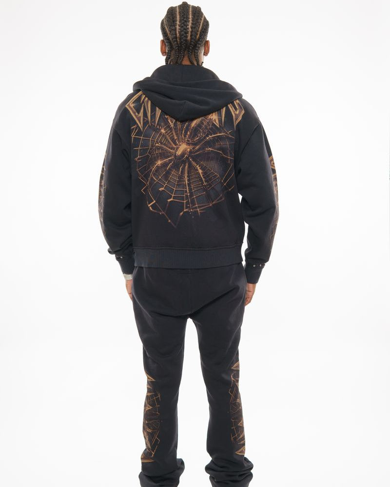 Person wearing a black hoodie and pants with a spider web design on a white background