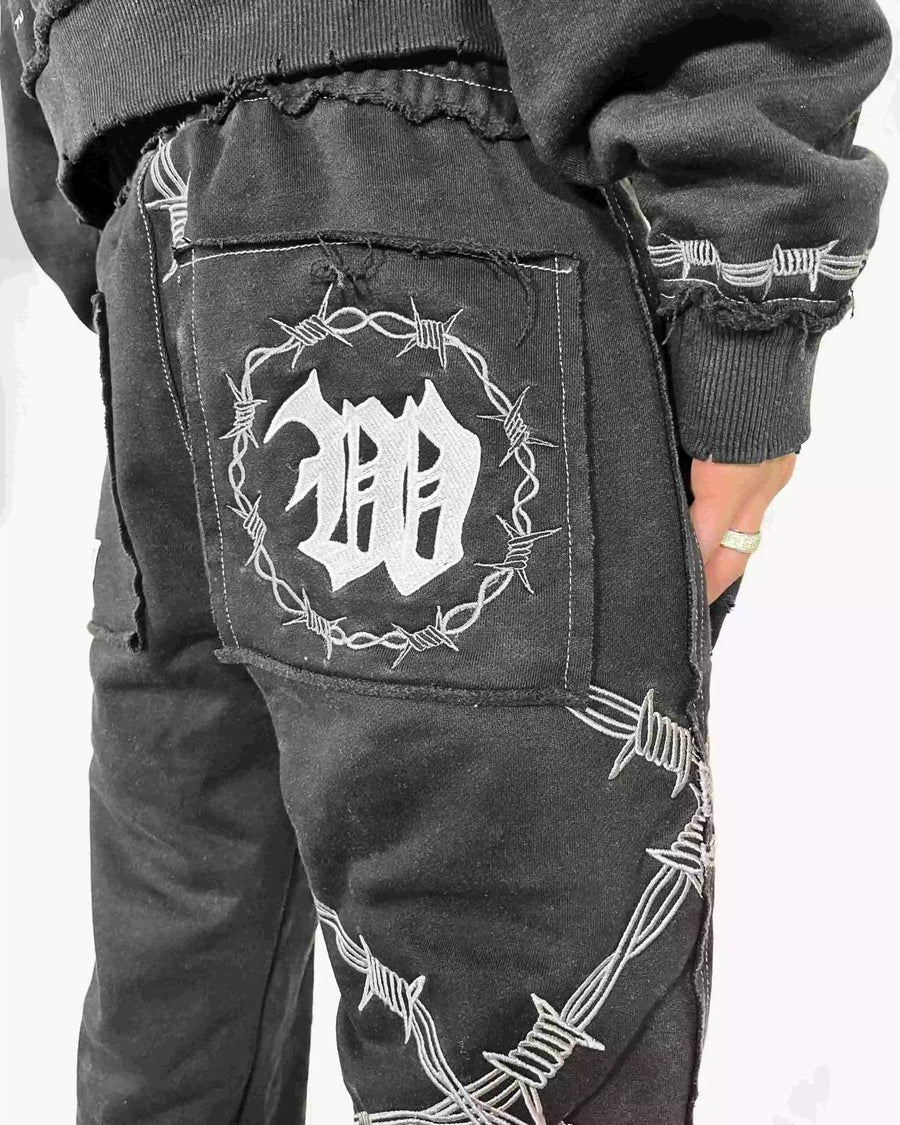 Black pants with barbed wire design and logo on a white background