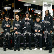 Five men wearing matching black outfits with white text standing in front of a Petro Canada gas station at night.