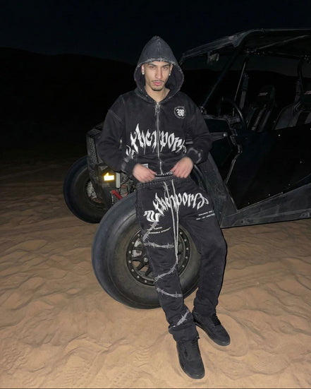 Person wearing a black hoodie with white text standing next to a vehicle in a desert setting at night.