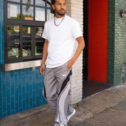 Man wearing a white t-shirt and gray pants standing outside a building with a blue tiled wall and red door.