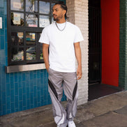 Man wearing a white t-shirt and gray pants standing in front of a colorful building.