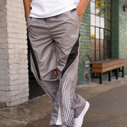 Person wearing gray pants with a brand logo, standing on a sidewalk.