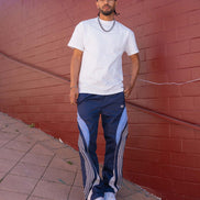 Man wearing a white t-shirt and blue tracksuit standing against a red brick wall.