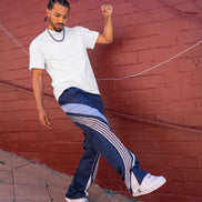 Man in white t-shirt and blue pants with white stripes dancing against a red brick wall.