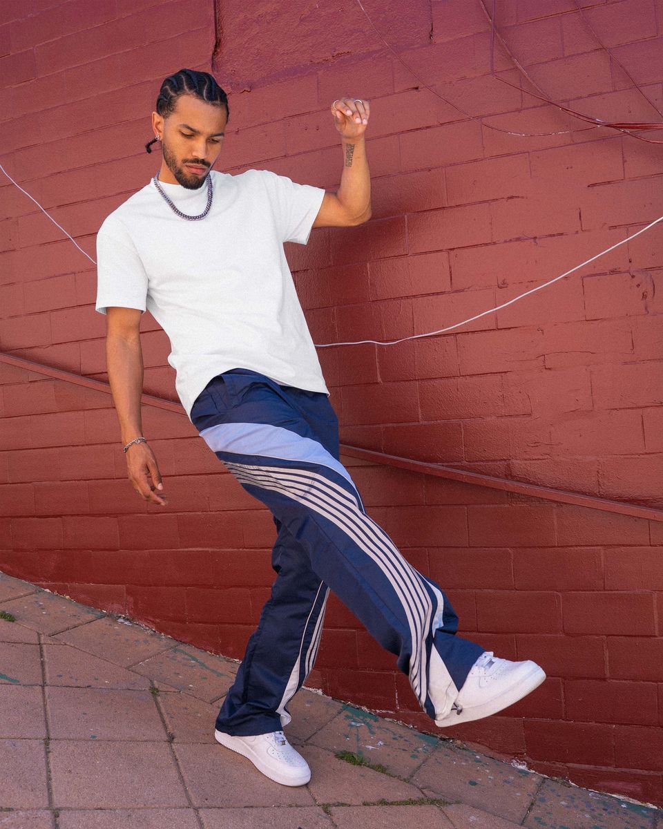 Man in white t-shirt and blue pants with white stripes dancing against a red brick wall.
