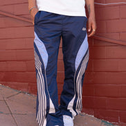 Person wearing navy track pants with white stripes against a red brick wall.