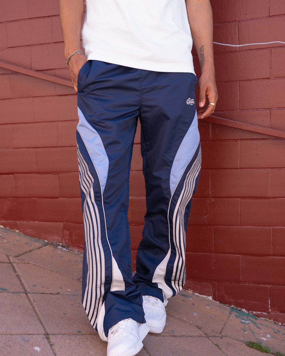 Person wearing navy track pants with white stripes against a red brick wall.