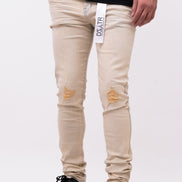 Beige distressed jeans with a brand label worn by a person on a white background
