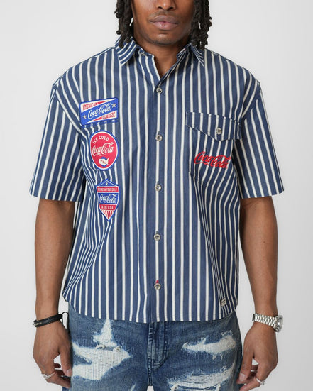 Person wearing a blue and white striped shirt with Coca-Cola logos on a white background