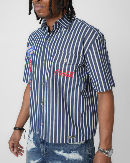 Person wearing a navy and white striped shirt with Coca-Cola logo on a plain background